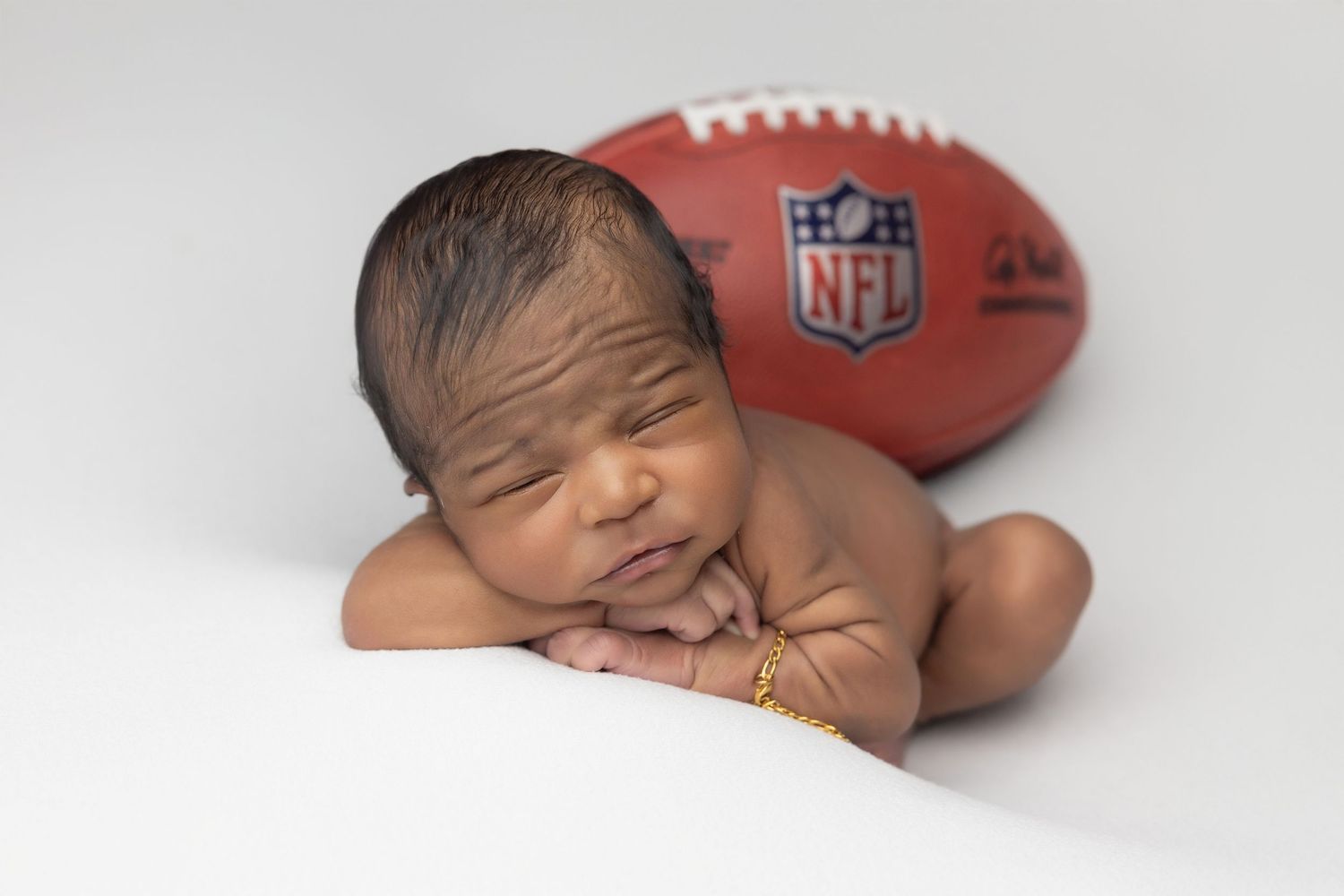 Newborn baby resting chin on hands inside a teal bucket with soft blanket, studio photography.
