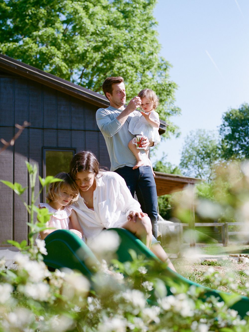 Happy family with two young children enjoying sunny day outside their modern dark-sided home.