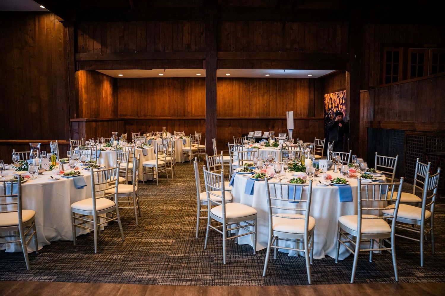 Elegant banquet hall with round tables, white linens, chiavari chairs, and floral centerpieces for a wedding reception.