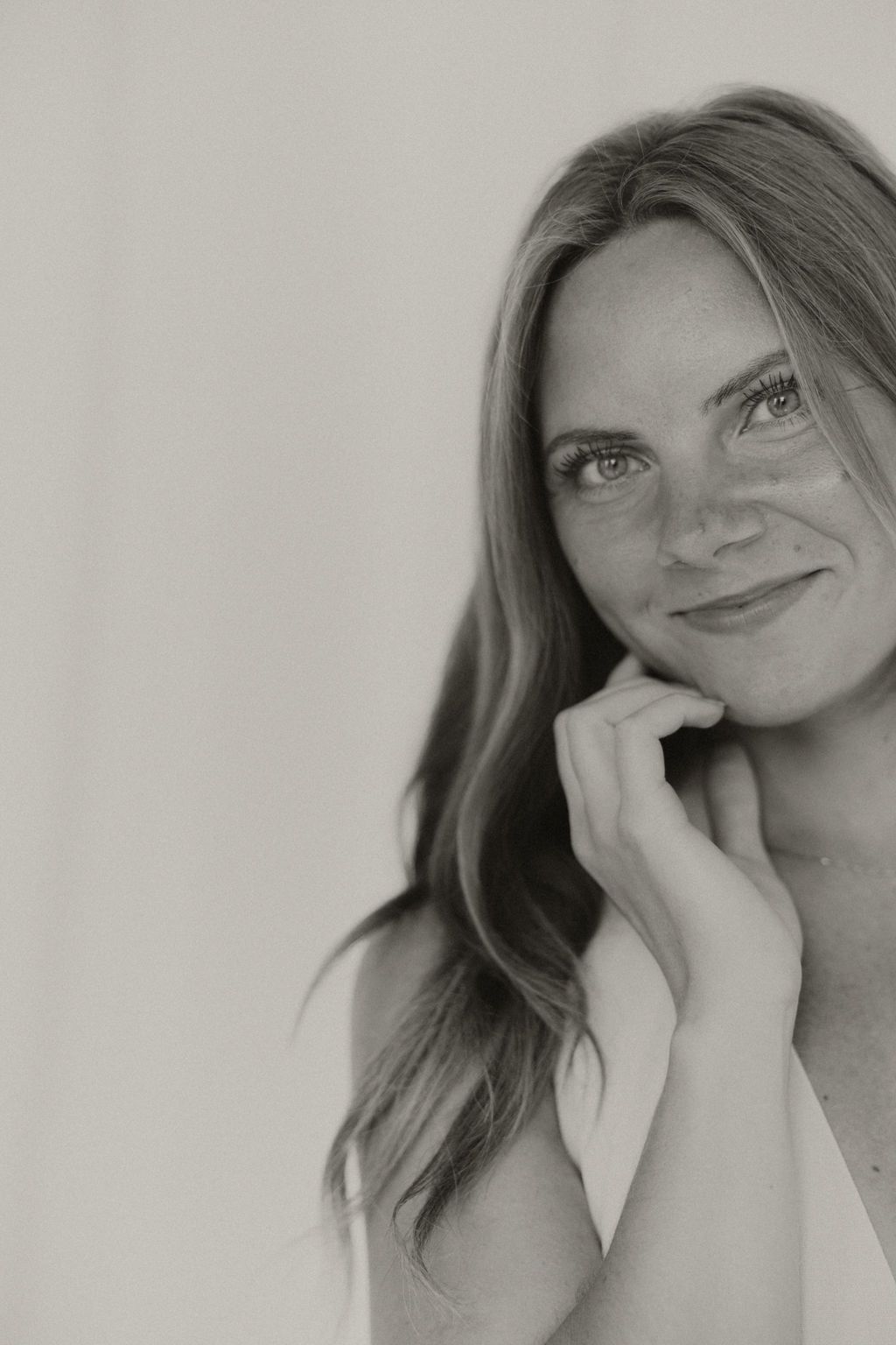 Black and white portrait of a smiling woman with long hair resting her chin on her hand.