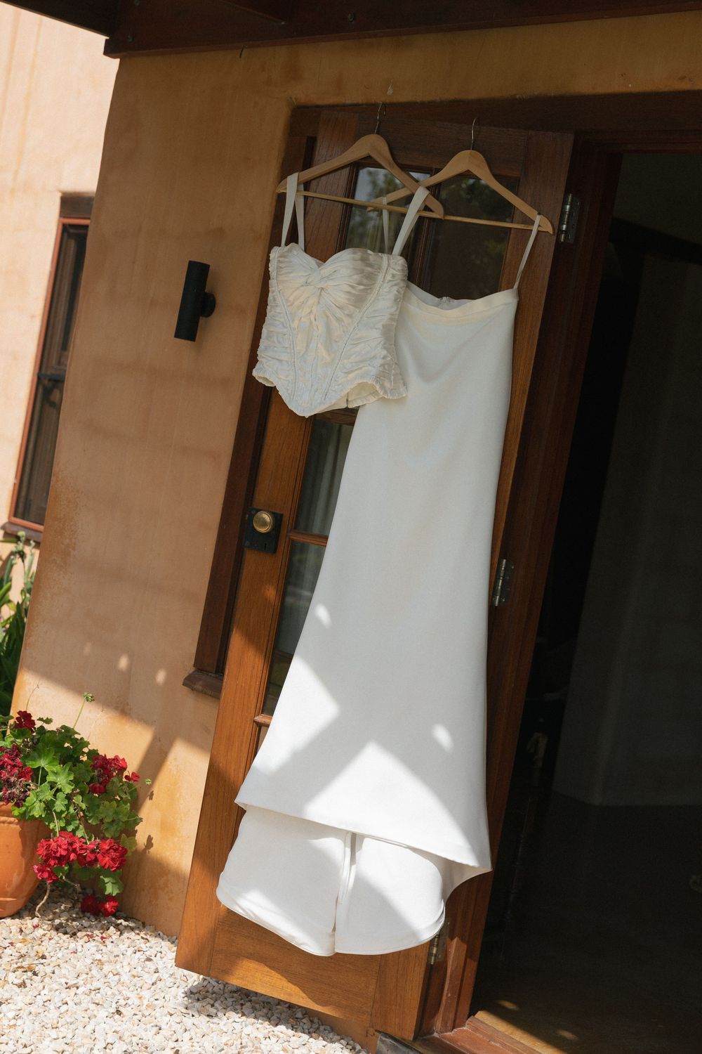 White wedding dress and embellished bodice hanging on wooden door at rustic outdoor venue.