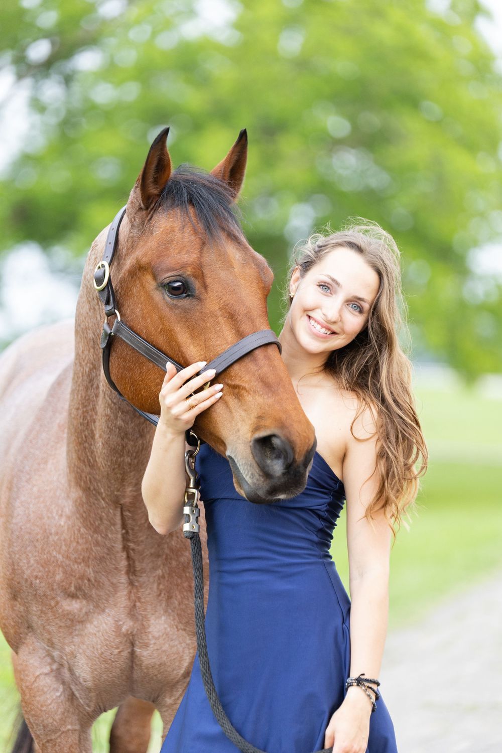 girl wearing navy blue dress standing next to a bay roam horse