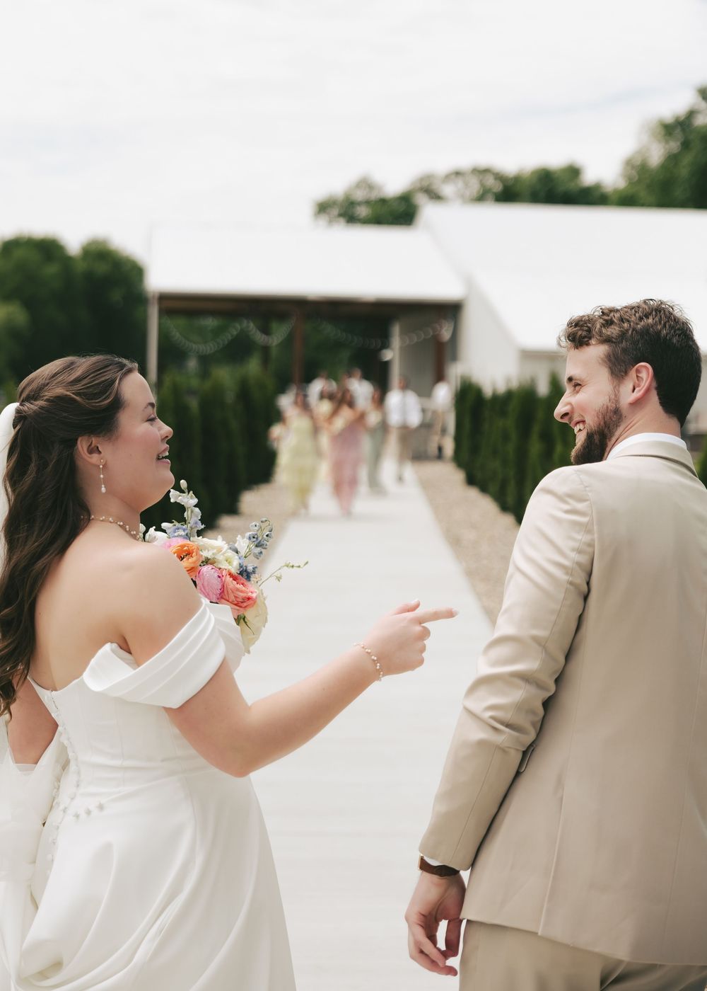 Bride and groom share a playful first look moment outdoors, smiling and pointing at each other on their wedding day.