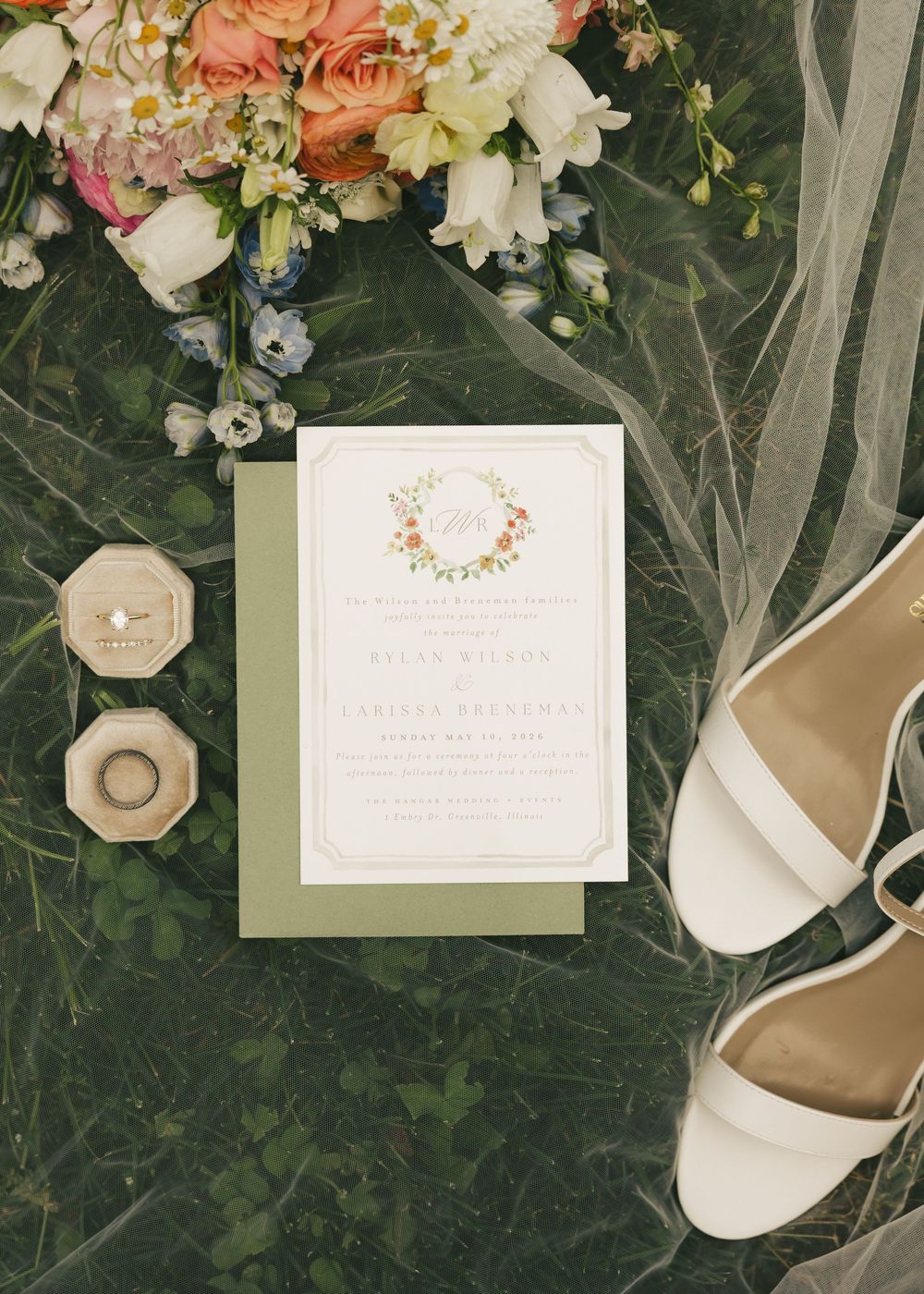 Close-up wedding flat lay with floral invitation, ring boxes, white heeled sandals, and a lush peach and pink bouquet.