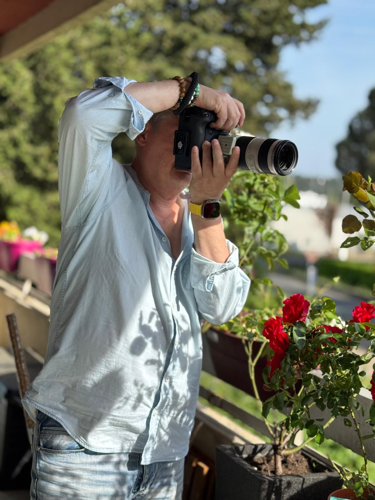 Photographer capturing images with a professional camera and telephoto lens on a sunny balcony with red roses.