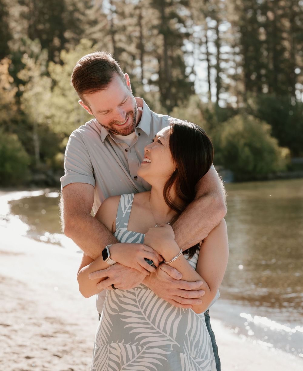 Happy couple embracing and laughing together on sunny beach with pine forest backdrop.