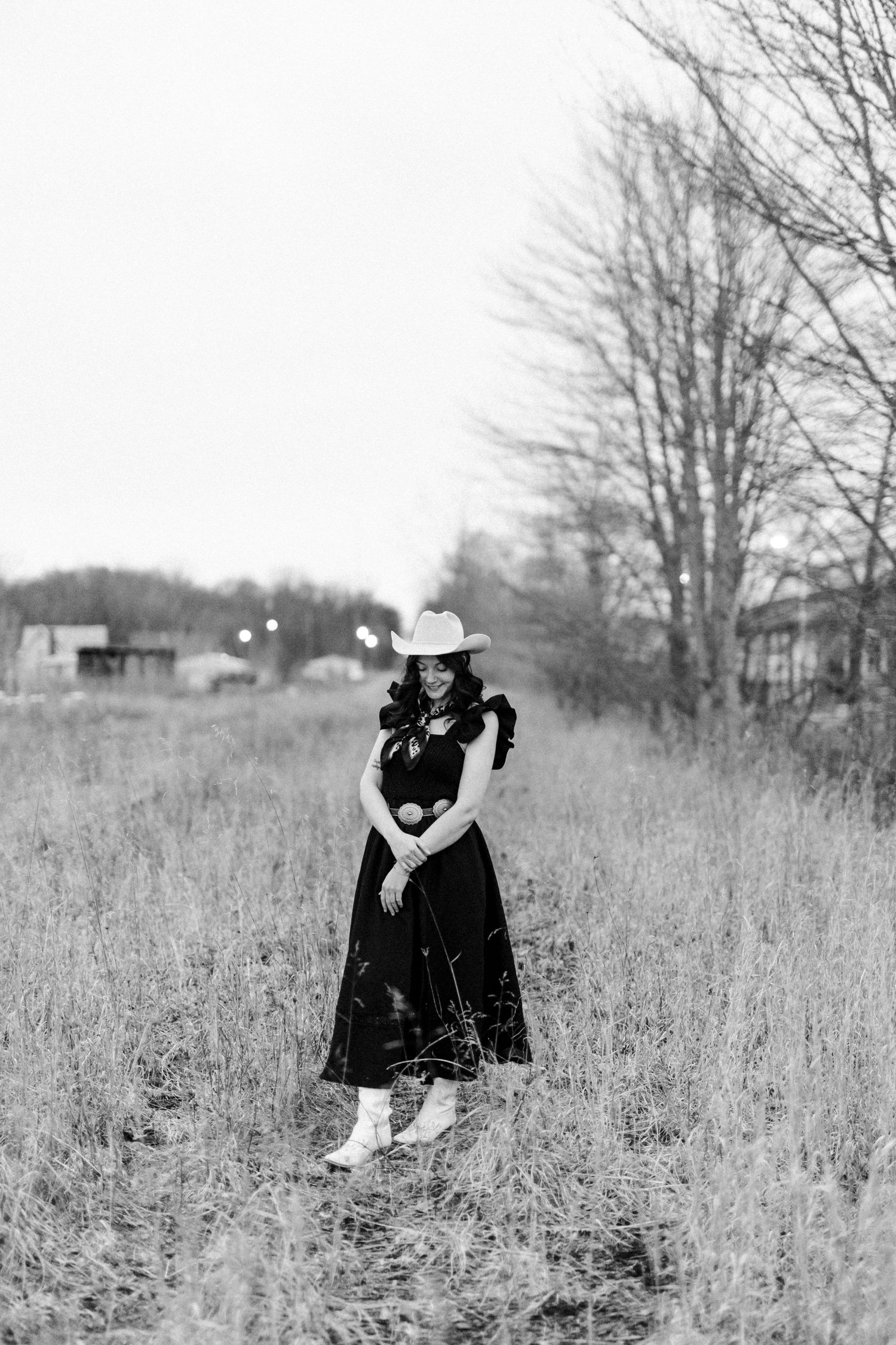 Young woman in white cowboy hat and red sunglasses poses outdoors in a black ruffled top.