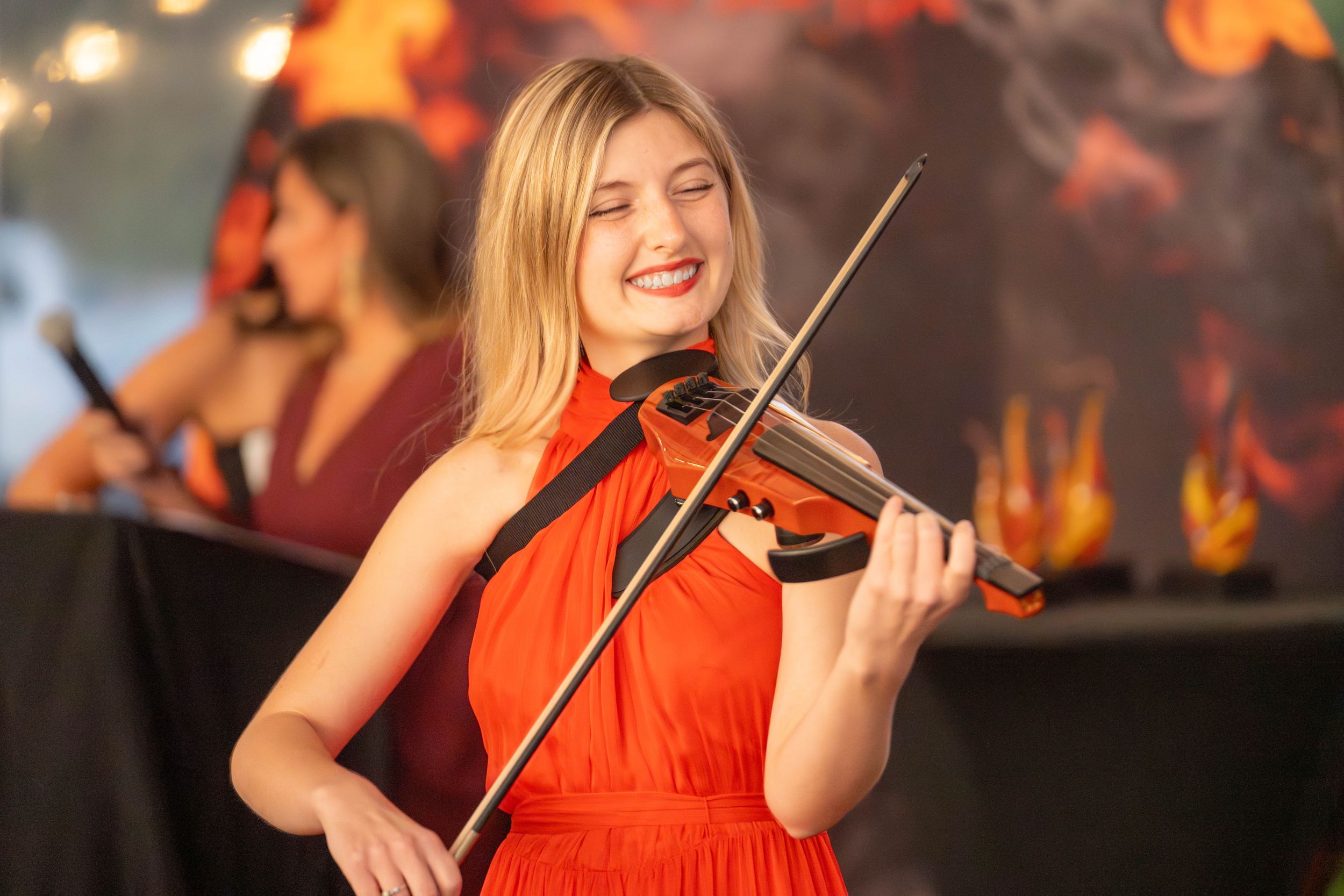 A musician in a bright red dress performs passionately on violin against a warm glowing background. Quad Cities Event Photography