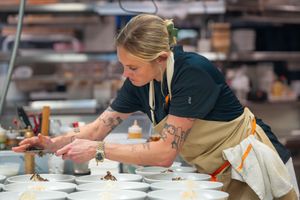 Chef in tan apron carefully plates an elegant fine dining dish in professional restaurant kitchen. Quad Cities Event Photography