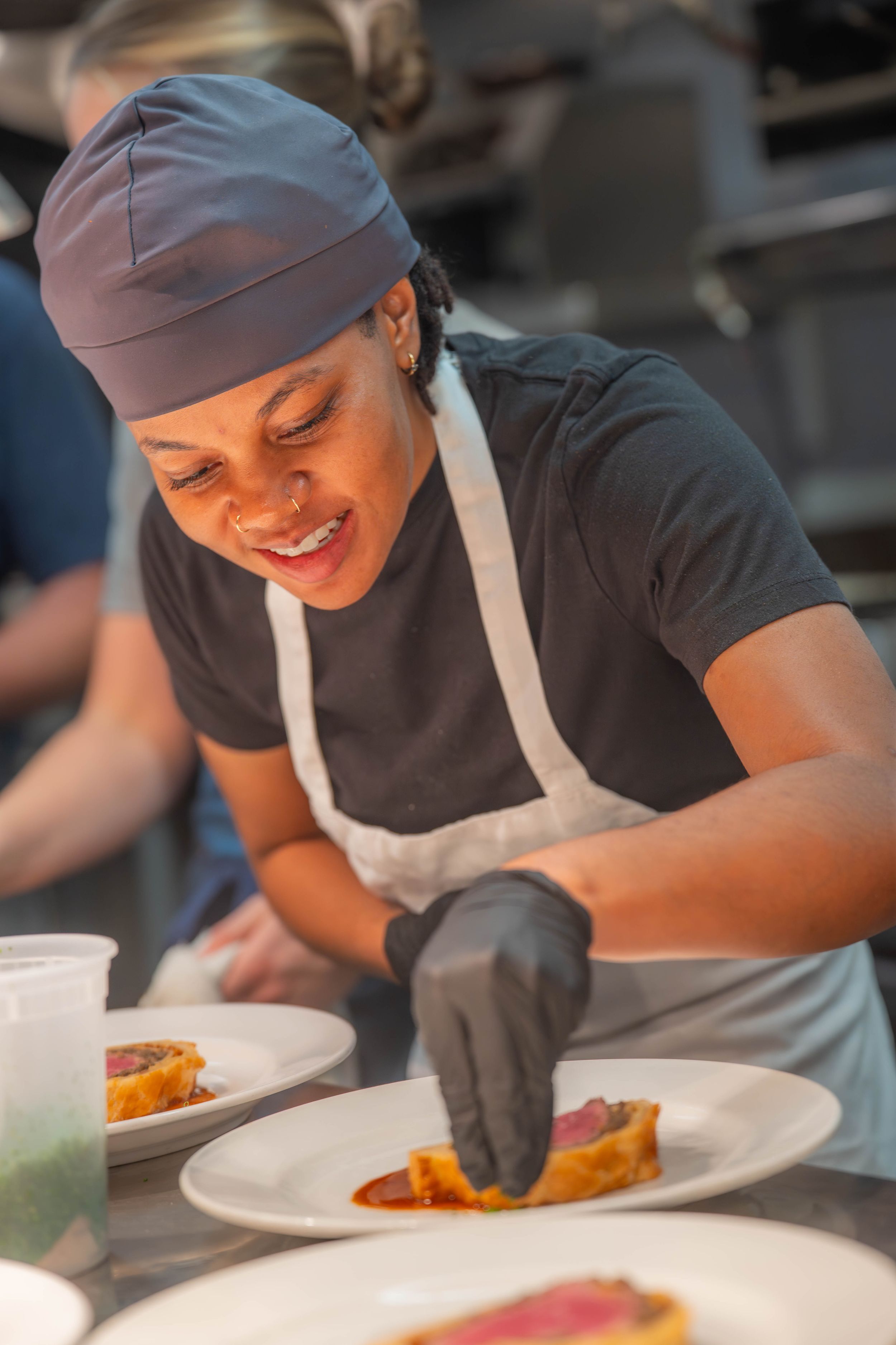 Chef in black uniform and hat carefully plates a colorful dish in professional kitchen setting. Quad Cities Event Photography