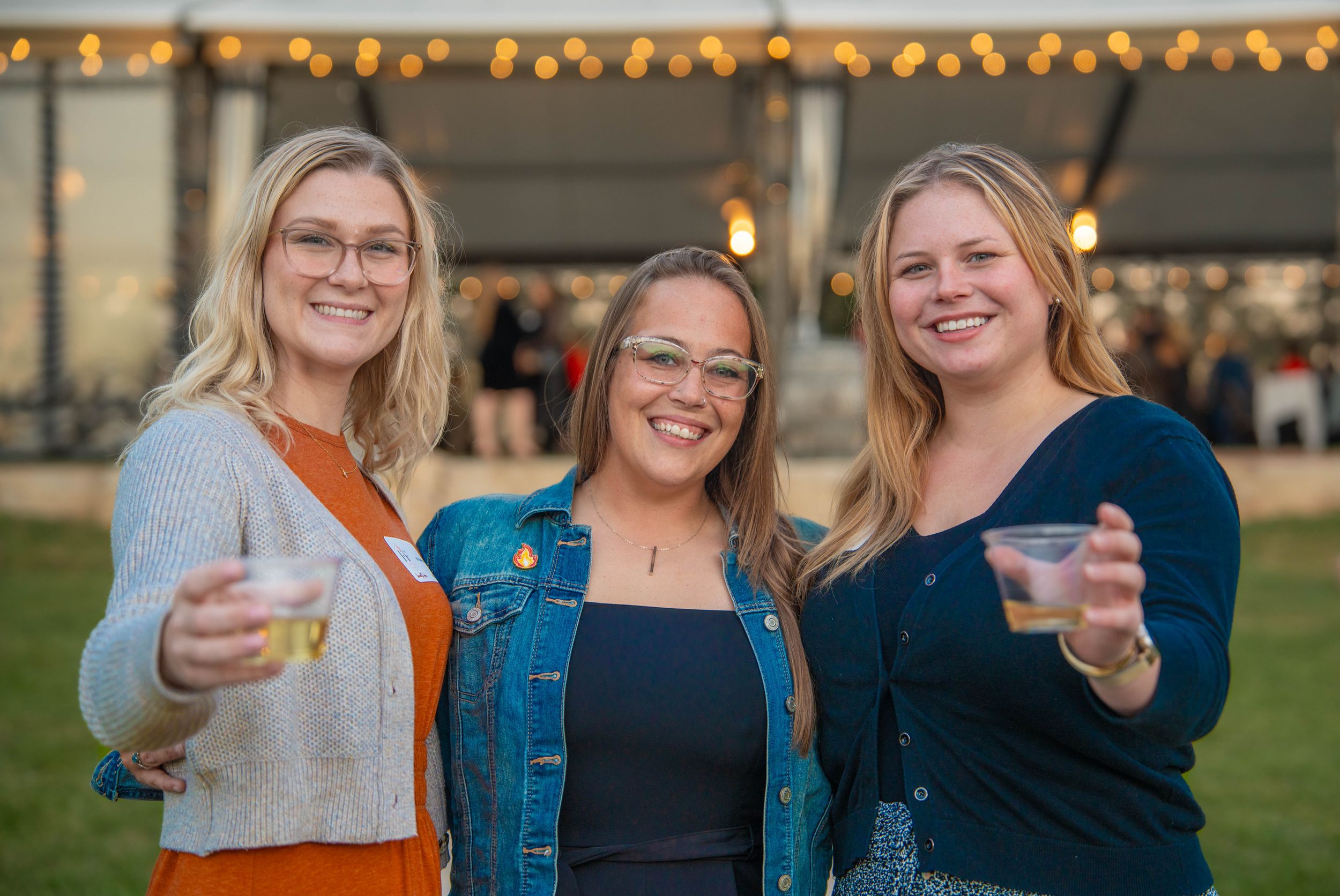 Group of friends enjoying drinks and giving thumbs up gestures at an outdoor gathering with string lights. Quad Cities Event Photography