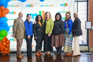 A group of professionals pose together against a blue and orange balloon backdrop at a corporate event.