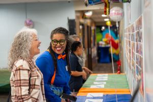 Two people having an engaging conversation while looking at displayed materials at a colorful indoor event.