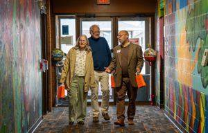 Three people walk through a colorful hallway decorated with vibrant wall murals.