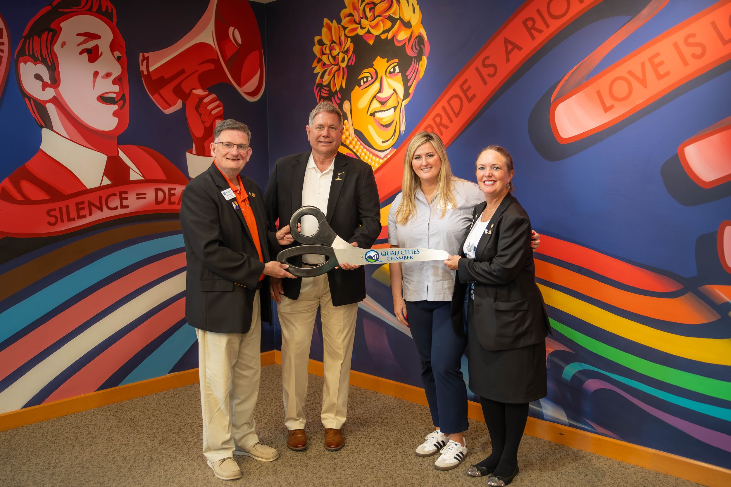 Group of people standing together holding awards in front of a colorful wall mural with megaphones and rainbow designs.