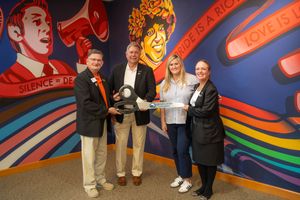 Group of people standing together holding awards in front of a colorful wall mural with megaphones and rainbow designs.