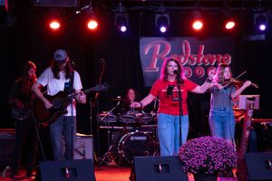Band performing on stage with red lighting and purple backdrop during live concert.