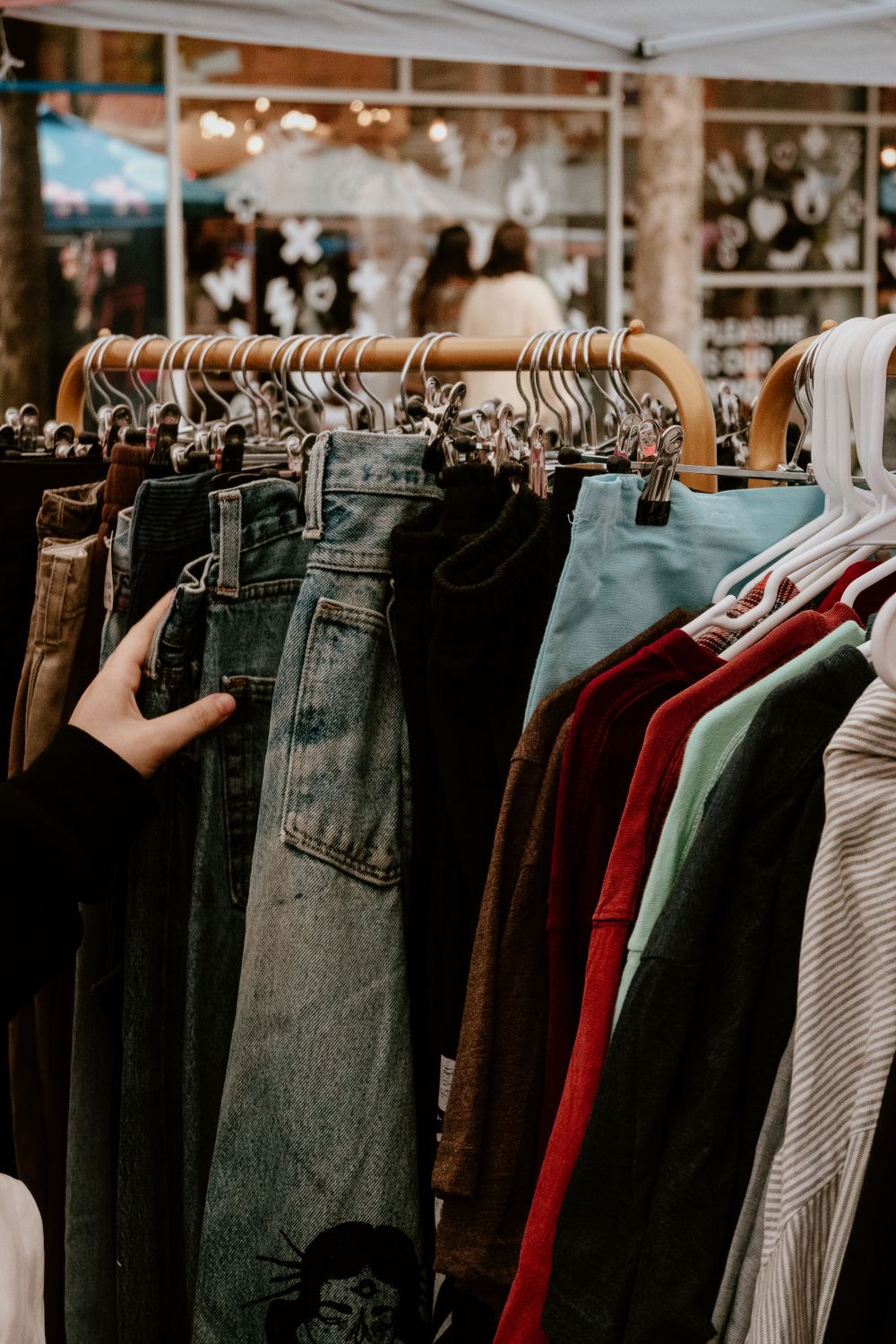 Clothing rack displaying a variety of denim jeans and casual wear at a market.