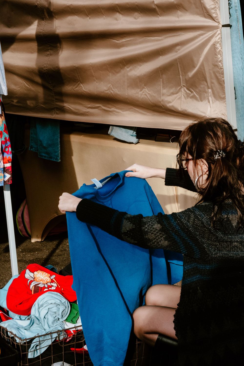 Person arranging clothing items under a beige market tent canopy.