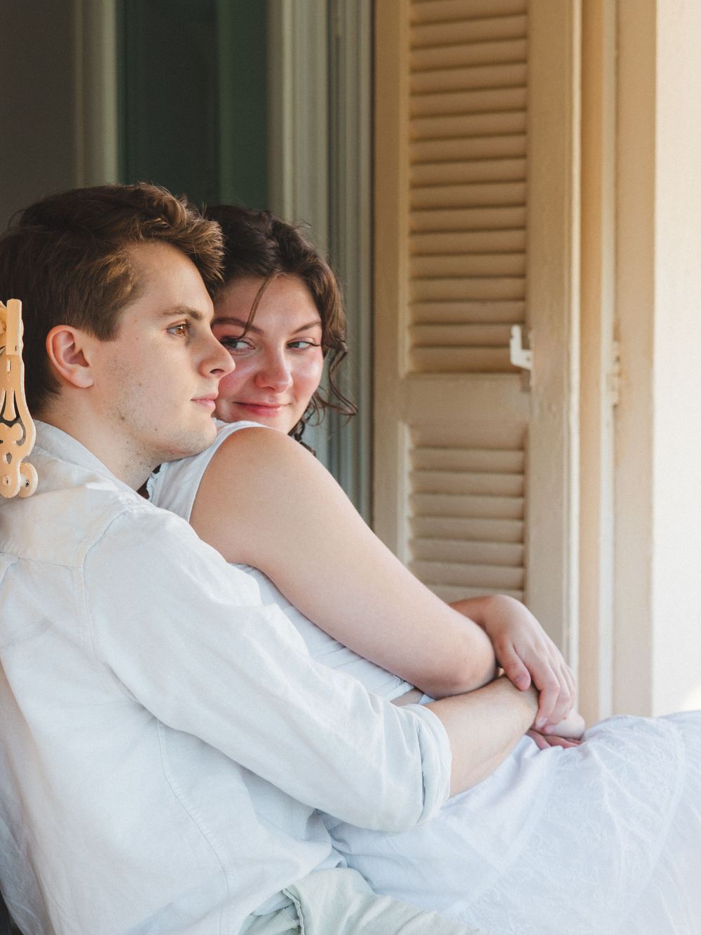 Young couple sitting together on a porch chair, sharing a tender moment outdoors.