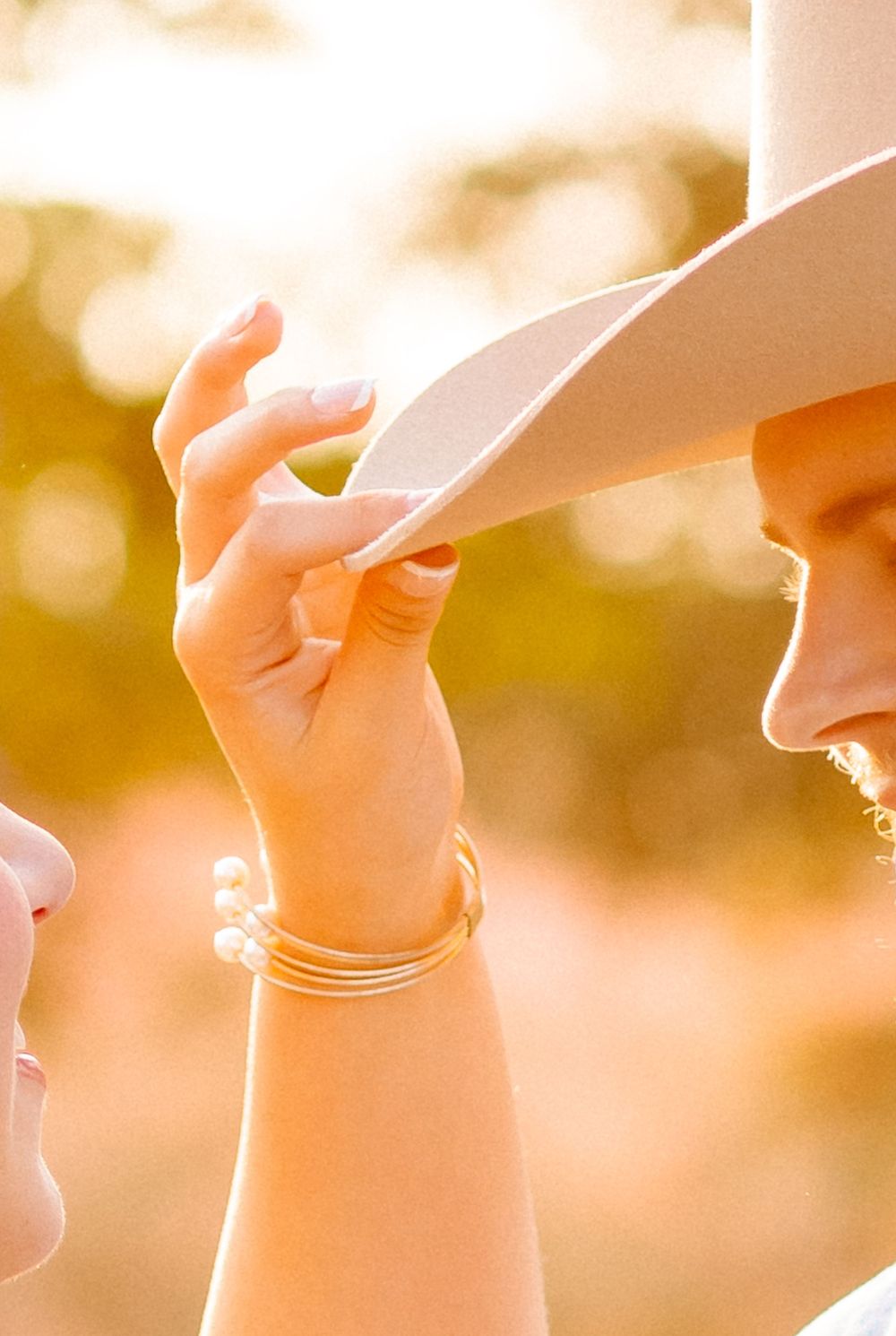 Close-up of a child reaching up to touch a woman's white cowboy hat in warm golden sunlight.