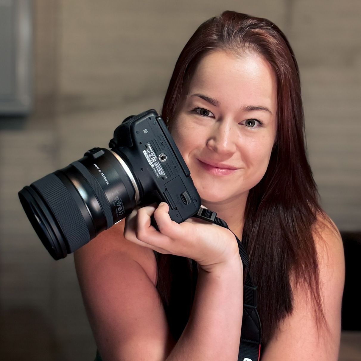Professional photographer poses with a mirrorless camera and zoom lens in a studio setting.