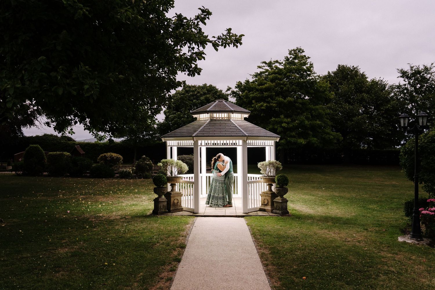 Groom standing in a white garden gazebo surrounded by lush greenery at a wedding venue The Batch Country House Wedding