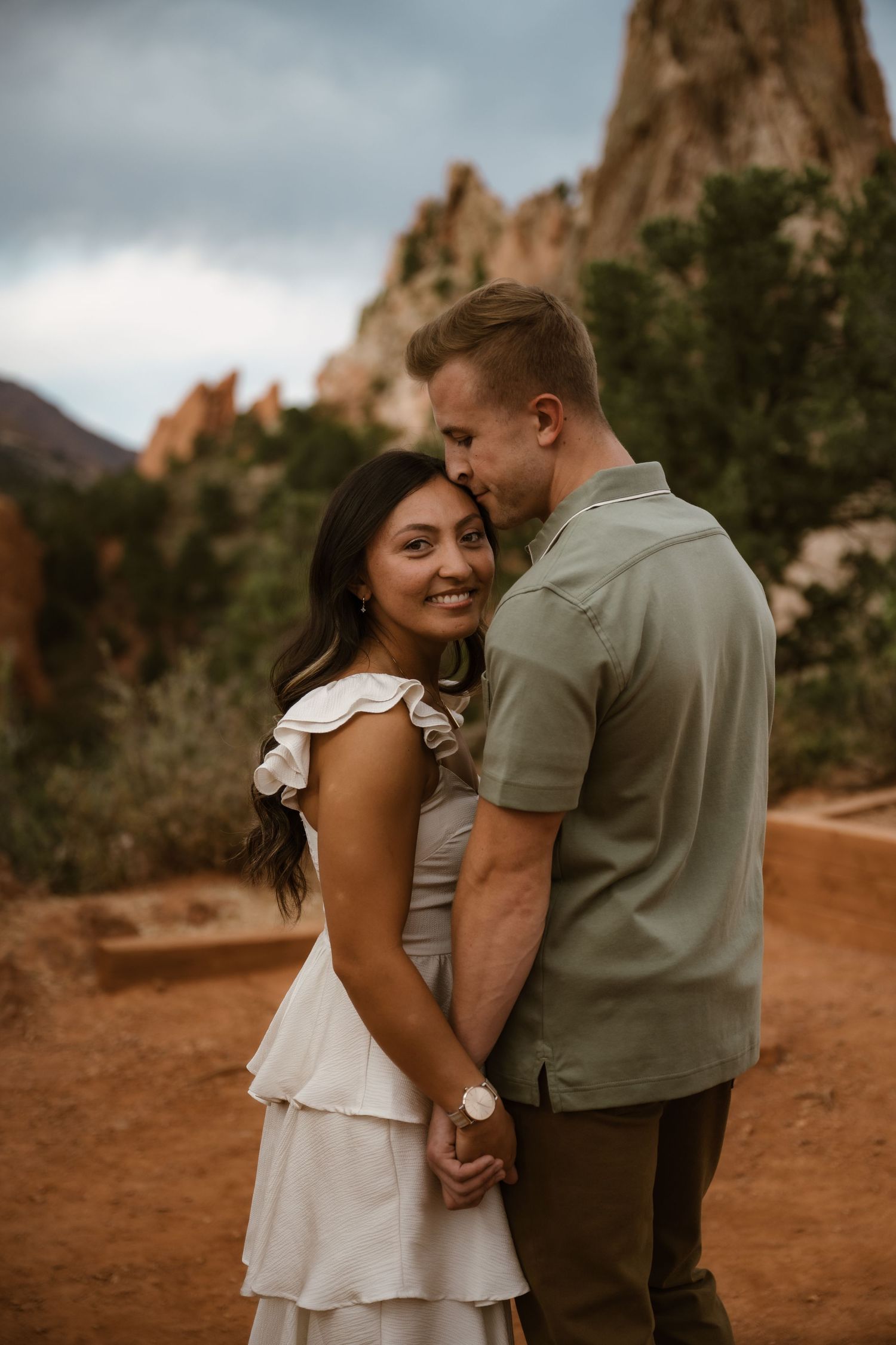 A couple shares an intimate moment against a backdrop of red rock formations in a desert landscape.