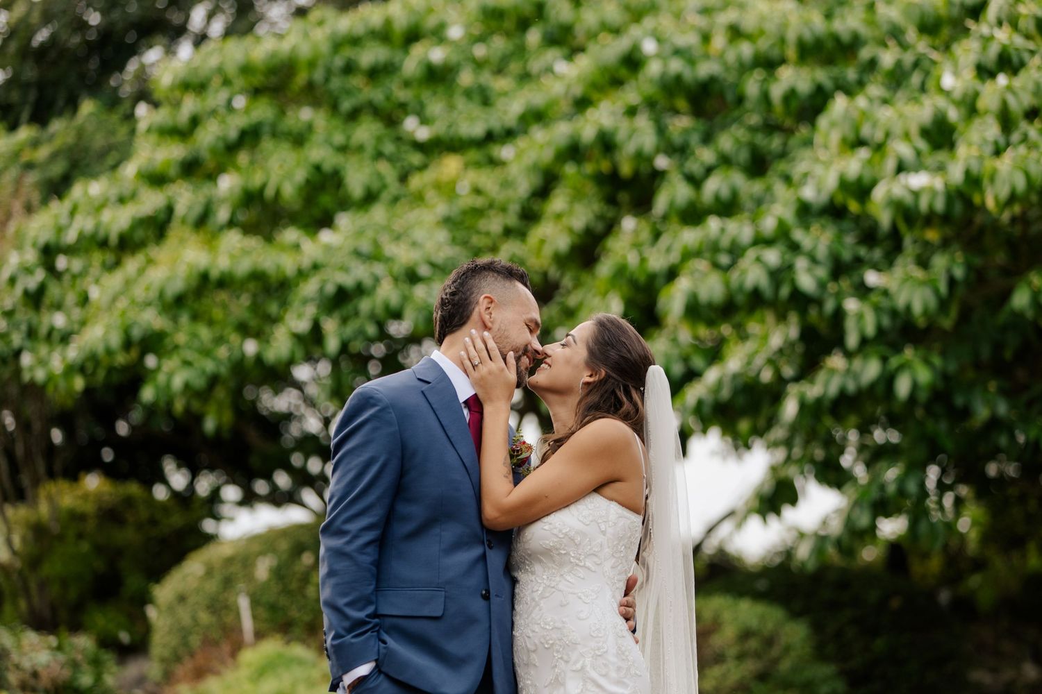 A tender wedding moment captured outdoors with lush greenery in the background.
