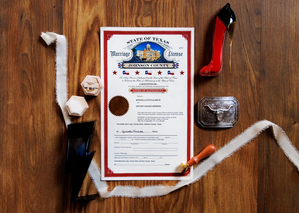 Wedding details flatlay with marriage certificate and decorative items on wooden surface.