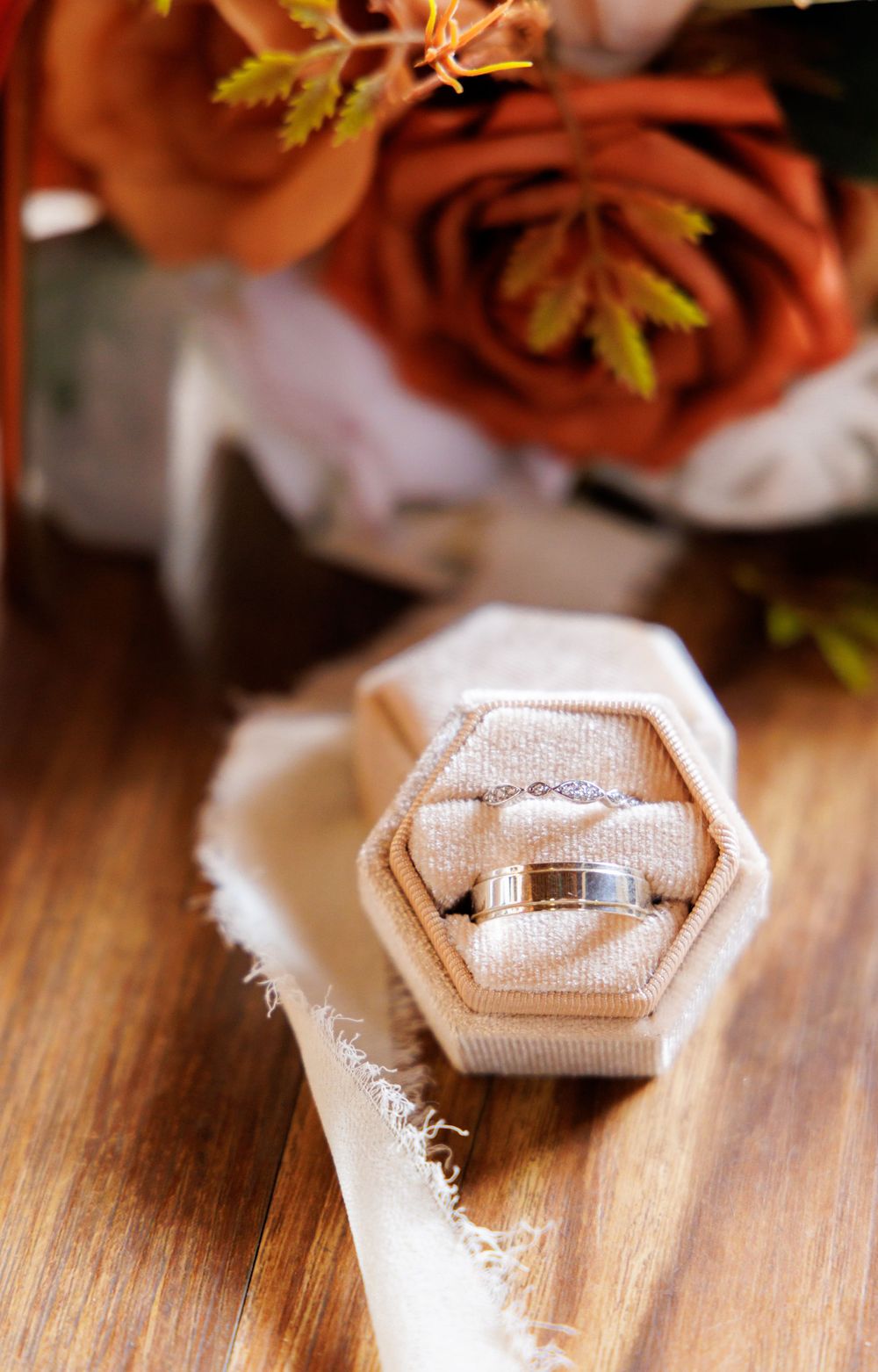 Wedding ring in hexagonal box with red roses on wooden surface.