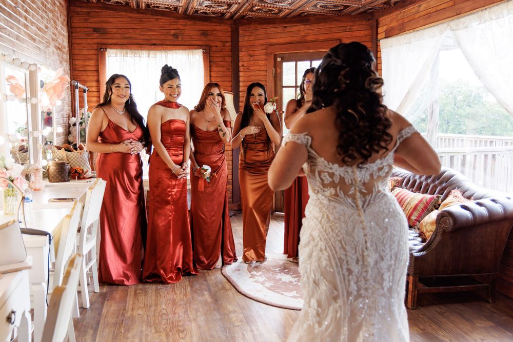 Wedding party scene with bridesmaids in rust-colored dresses in rustic venue.