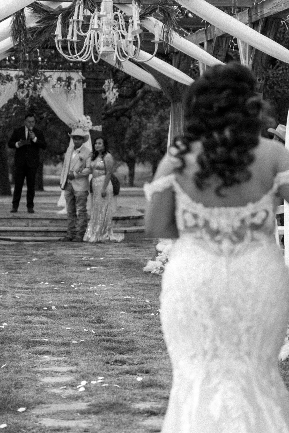 Black and white wedding ceremony photo with chandelier and outdoor setting.