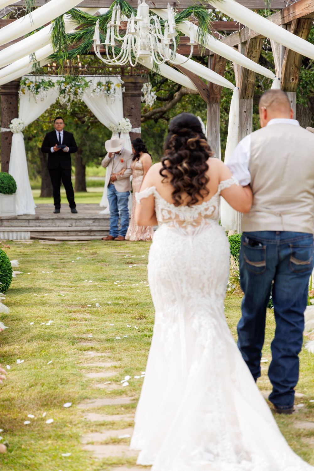 Elegant outdoor wedding ceremony under draped white canopy with hanging chandelier and greenery decorations.