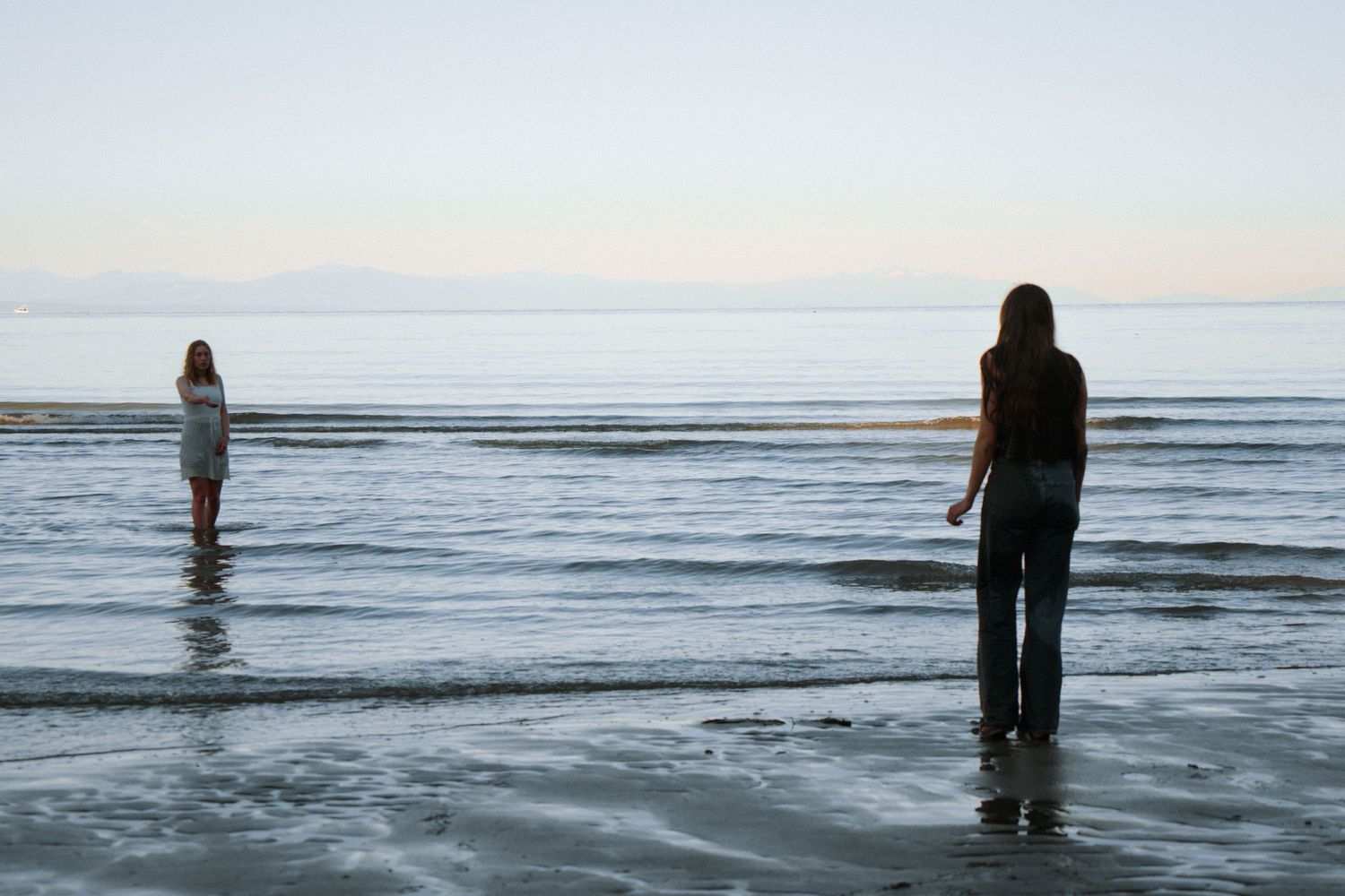 Two silhouetted figures standing in shallow ocean waters during sunset.