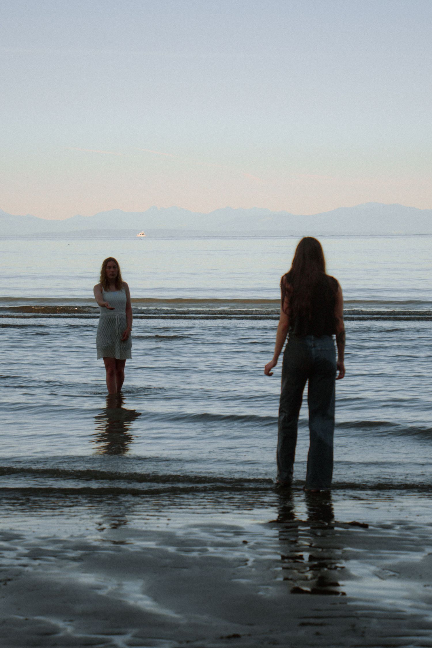 Two people standing in shallow ocean waters with misty mountains visible on the horizon.