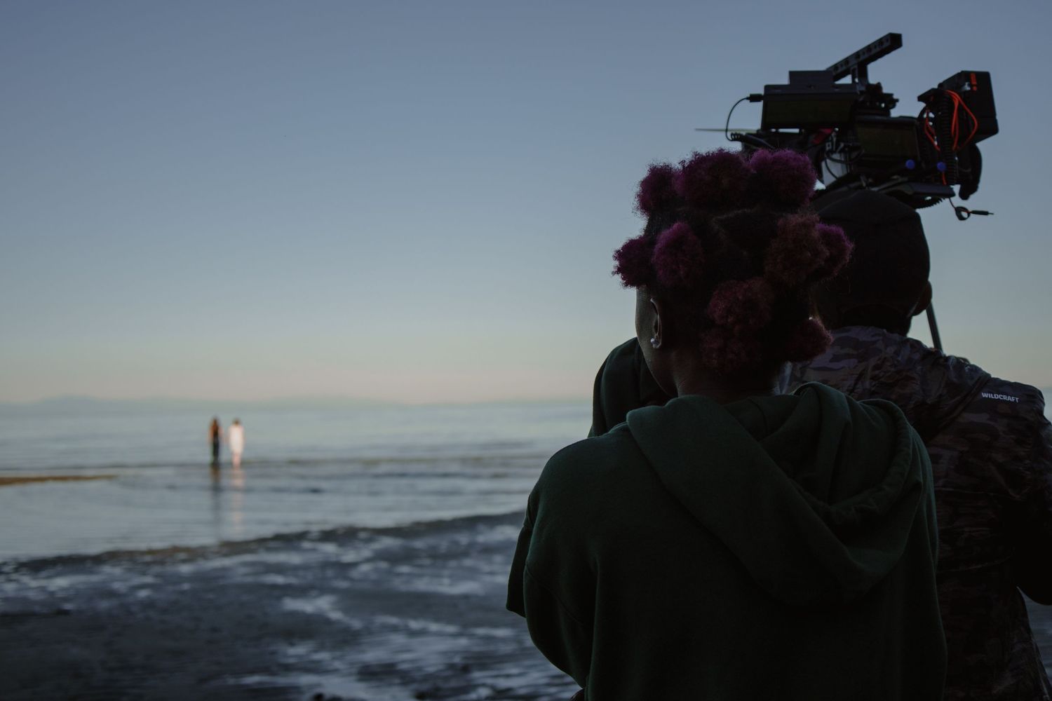 Camera operator filming at the beach during sunset.