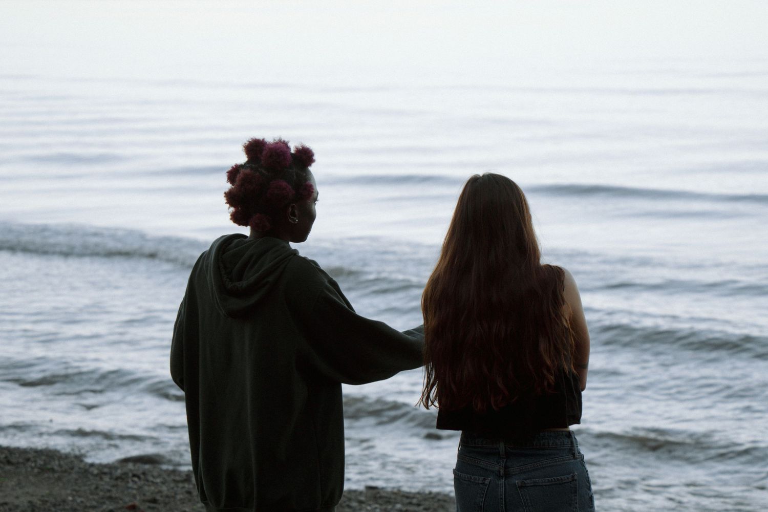Two figures watching the ocean waves at dusk with one wearing hair curlers.