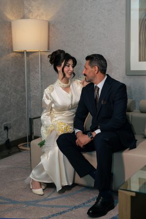 A couple in wedding attire shares intimate moments while sitting on a couch in an elegant room.