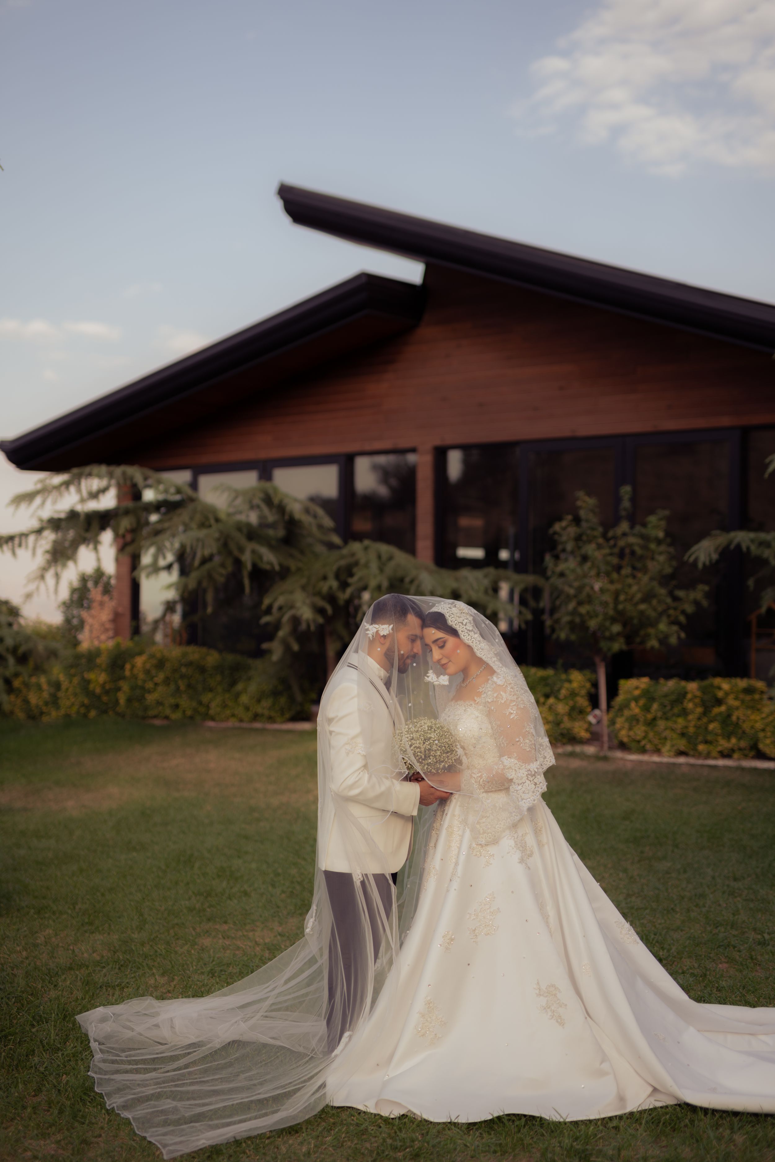 Wedding couple embracing under a flowing veil against a rustic wooden building backdrop.