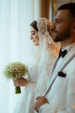 Side profile of wedding couple with baby's breath bouquet against window light.