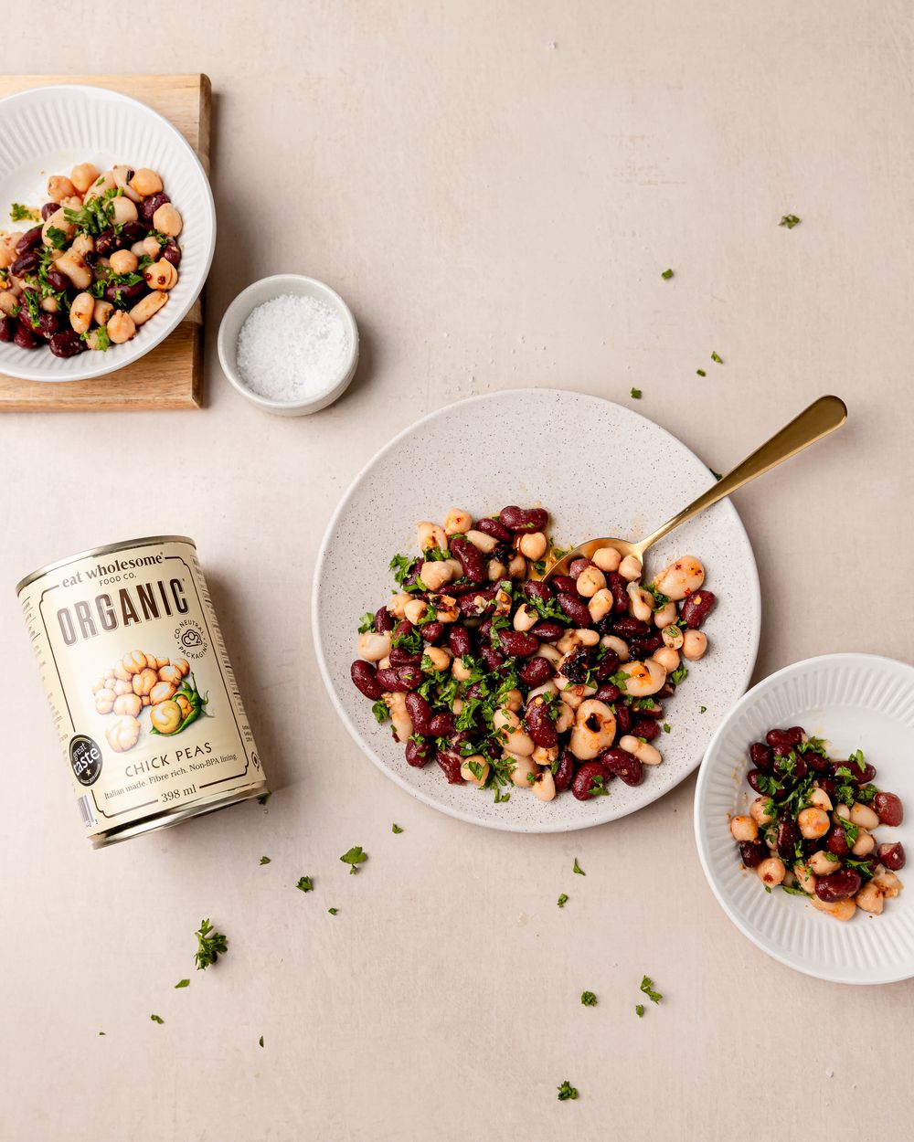 Chickpea and kidney bean salad with herbs on ceramic plates, styled with Eat Wholesome can on a neutral background.
