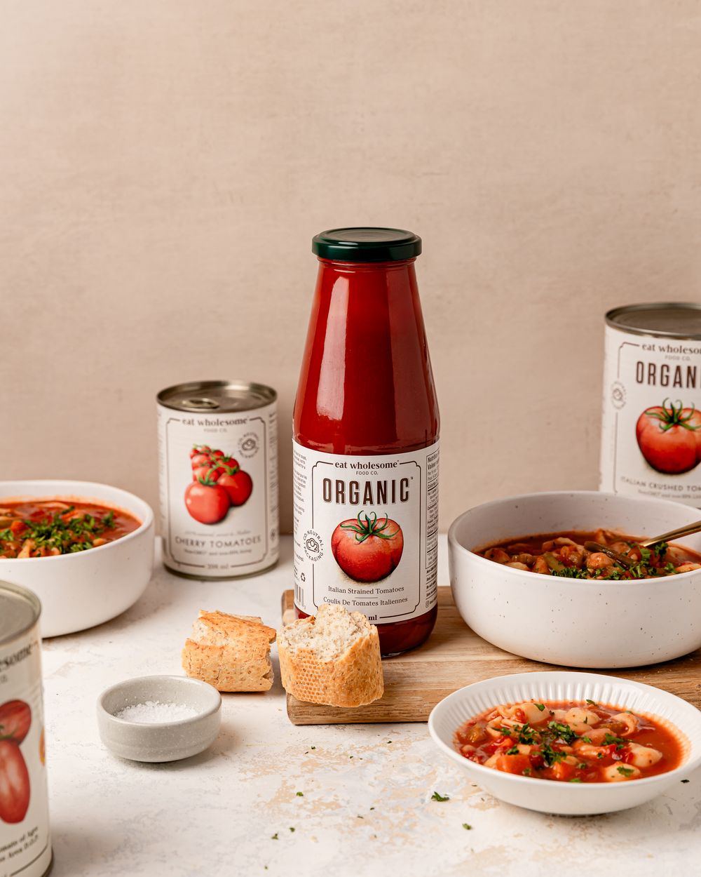 Tomato soup with bread and Eat Wholesome tomatoes styled on a neutral background in soft natural light.