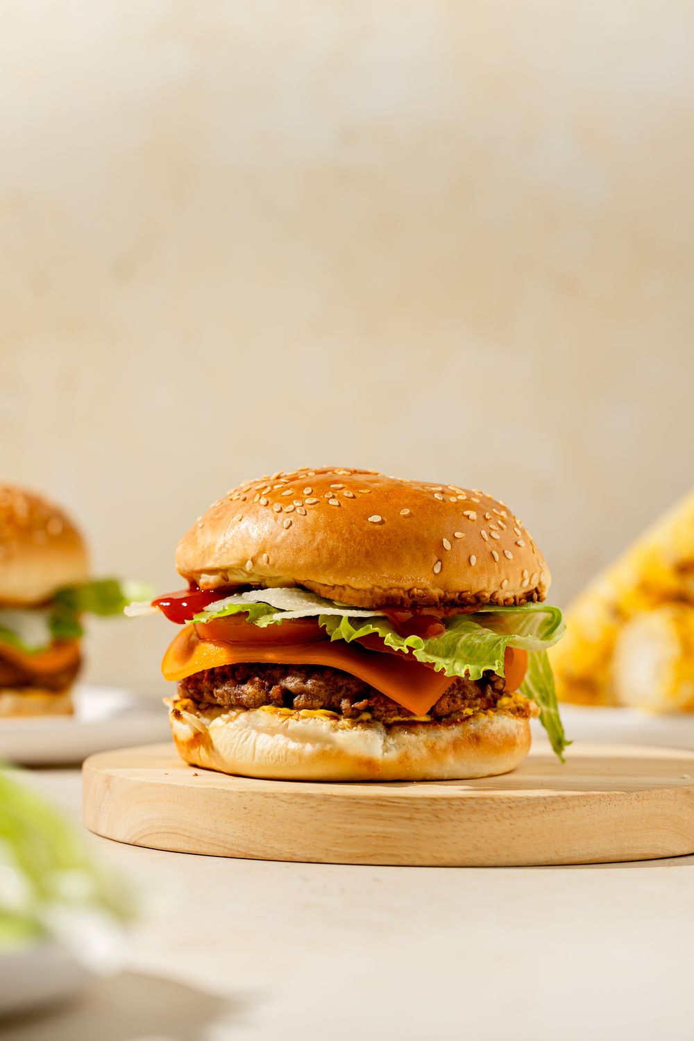Vegan cheeseburger with lettuce, tomato, and melted cheese on a sesame bun, styled on a wooden board in soft light.