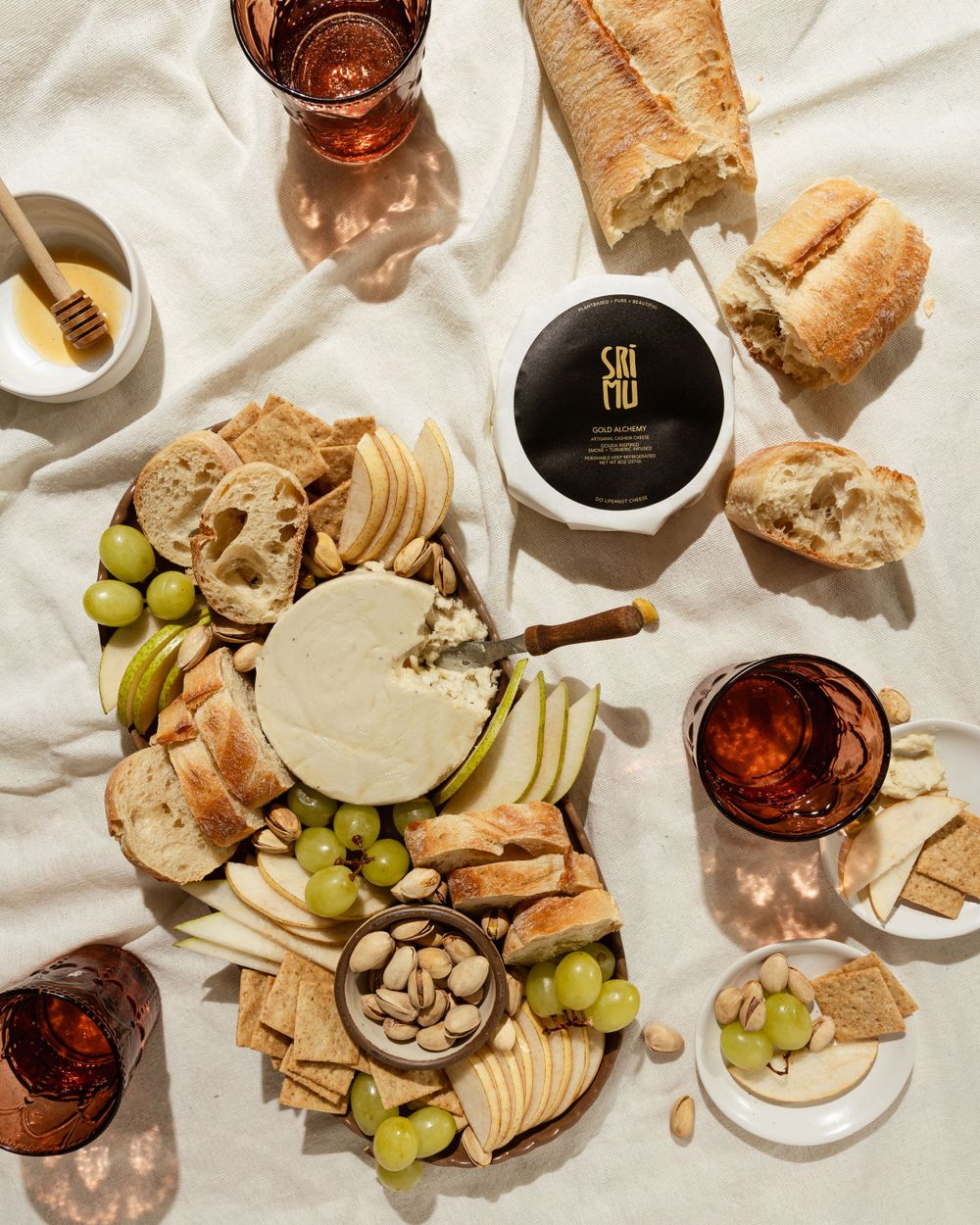 Grazing board with pear, Asian pear, baguette, almond crackers, pistachios, and vegan truffle cheese on a linen backdrop.
