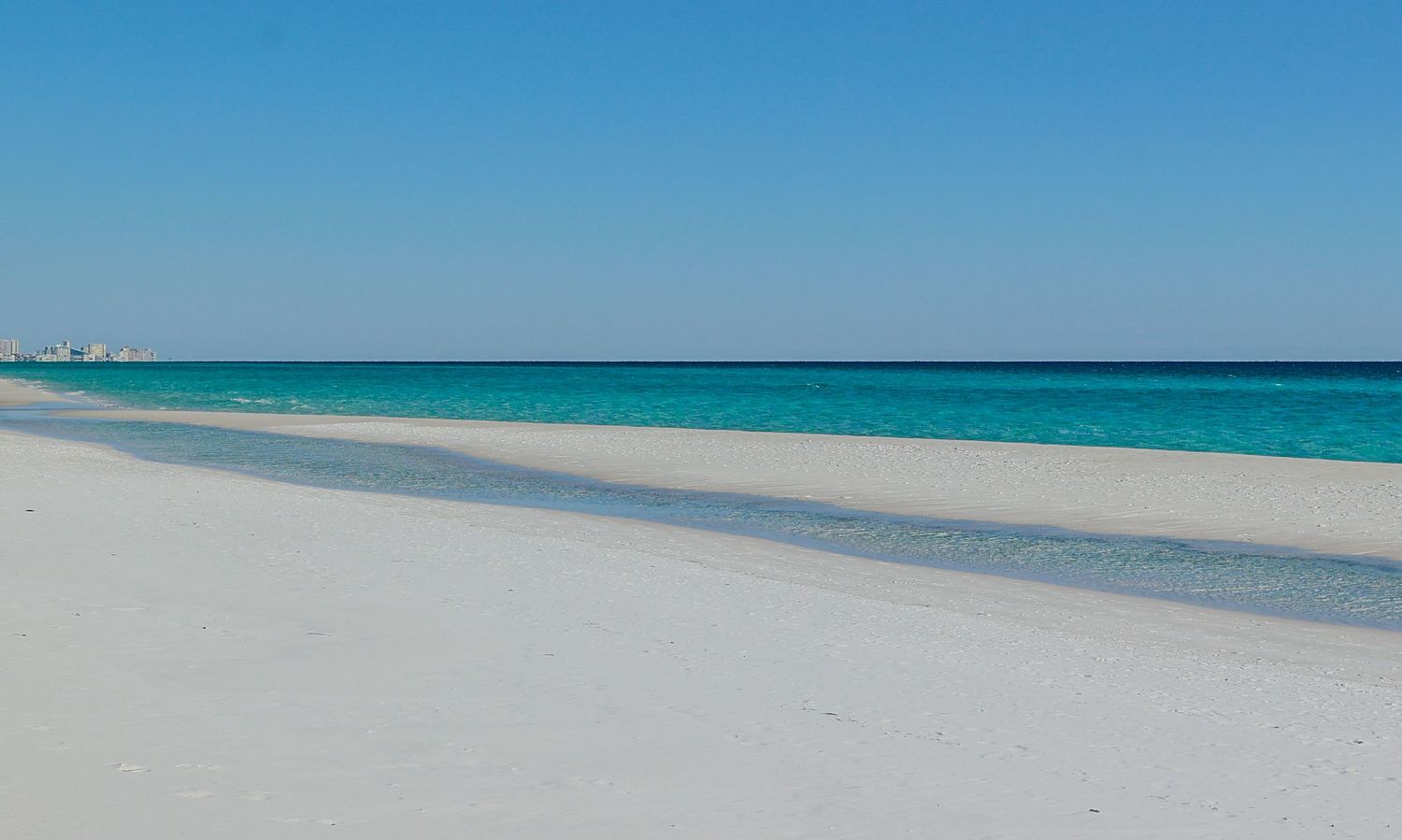 Pristine white sand beach meets turquoise waters under clear blue skies along a tranquil tropical coastline.