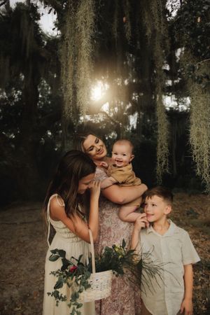 A family poses together under Spanish moss hanging from trees at sunset creating a dreamy outdoor portrait.