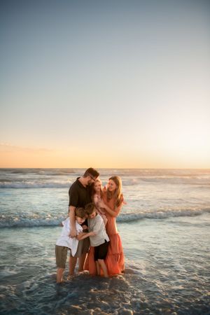 A family stands together in shallow ocean waves at sunset creating a tender beach moment.