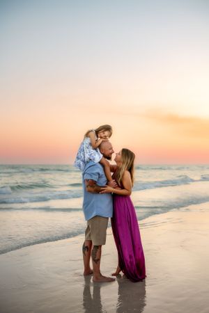 A loving family stands together on the beach at sunset as gentle waves lap at their feet in an intimate moment.