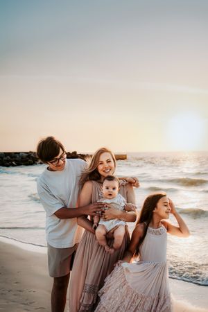 A joyful family enjoys a warm sunset together at the beach with waves and rocks in the background.